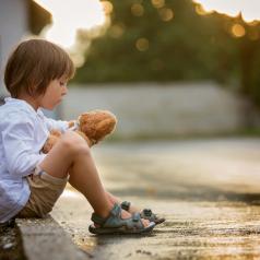Child sitting on step with stuffed toy at sunset