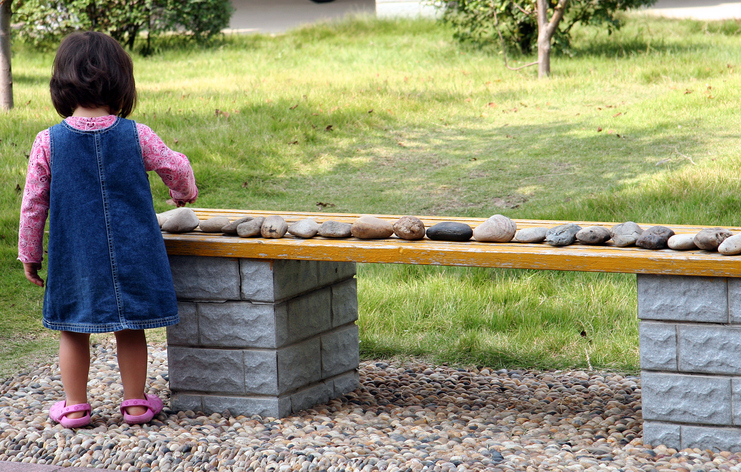 A young girl lines up all the rocks in the yard on a bench.