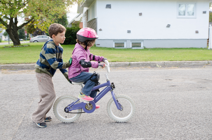 A young boy teaches his sister how to ride a bike.