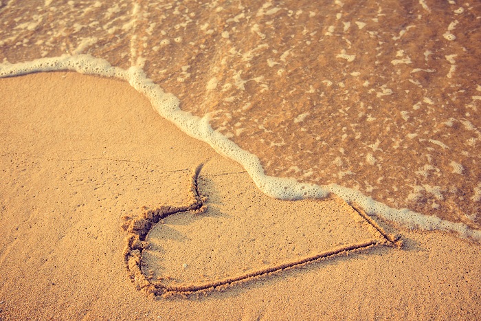 Waves washing away a heart that was drawn in the sand at the beach