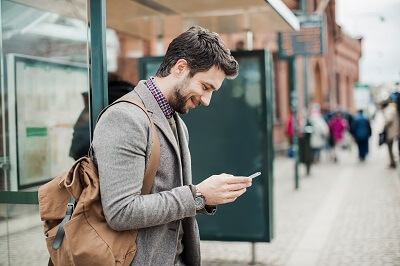 Professional man with bag over shoulder looking at phone at bus stop