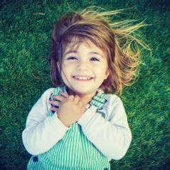 Overhead view of smiling child lying back on field of grass with hands over heart